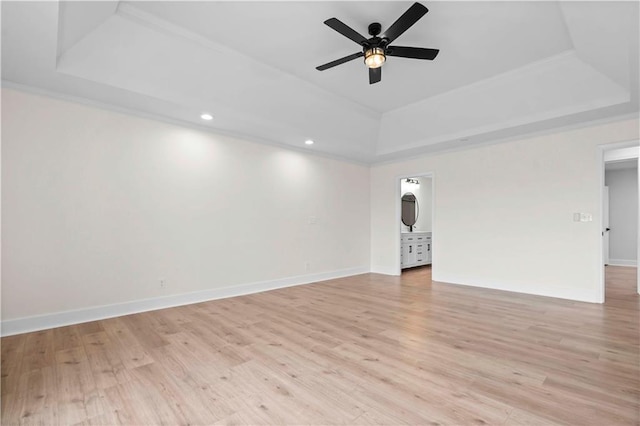 unfurnished room with a tray ceiling, baseboards, and light wood finished floors