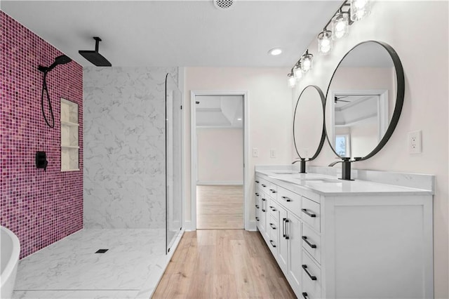 full bathroom featuring double vanity, wood finished floors, a sink, and tiled shower