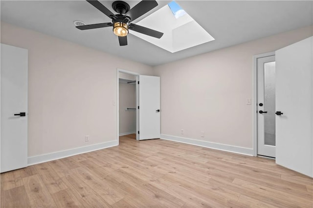 unfurnished bedroom with ceiling fan, light wood finished floors, a skylight, and baseboards