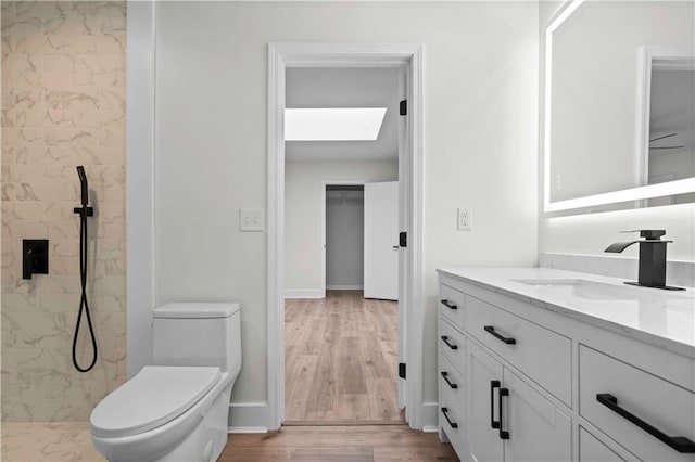 bathroom featuring a skylight, tiled shower, toilet, wood finished floors, and vanity