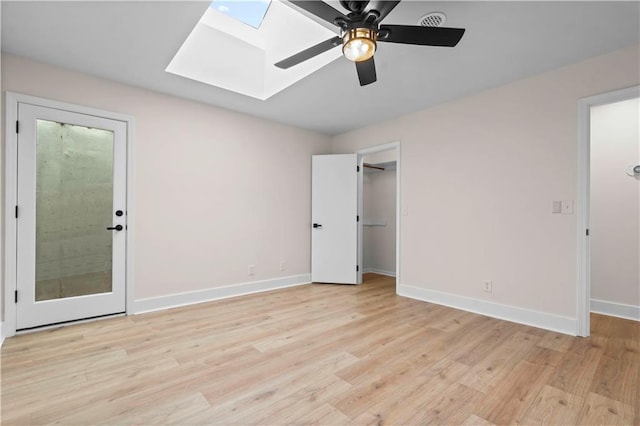 unfurnished bedroom with a skylight, baseboards, a spacious closet, and light wood finished floors