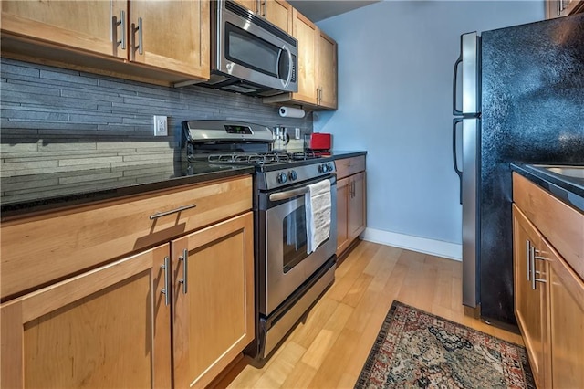 kitchen featuring stainless steel appliances, dark stone countertops, light hardwood / wood-style floors, and decorative backsplash