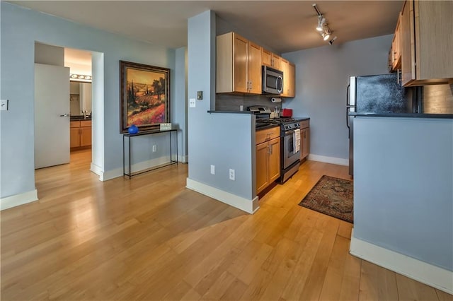 kitchen with rail lighting, appliances with stainless steel finishes, backsplash, and light hardwood / wood-style flooring