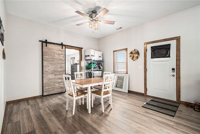 dining space featuring hardwood / wood-style flooring, ceiling fan, and a barn door