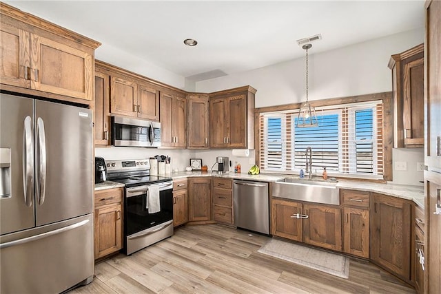 kitchen with appliances with stainless steel finishes, pendant lighting, sink, light stone counters, and light hardwood / wood-style flooring