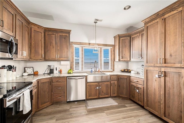 kitchen with sink, light hardwood / wood-style flooring, pendant lighting, stainless steel appliances, and light stone countertops