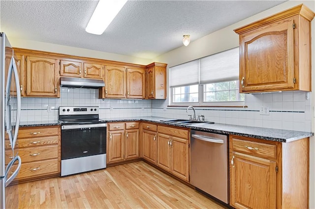 kitchen with sink, light hardwood / wood-style flooring, appliances with stainless steel finishes, decorative backsplash, and dark stone counters