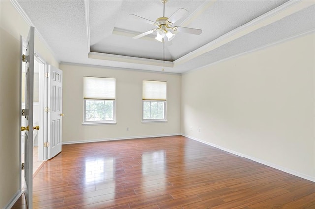 empty room featuring wood-type flooring, ornamental molding, ceiling fan, a tray ceiling, and a textured ceiling