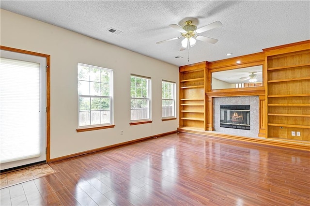 unfurnished living room featuring wood-type flooring, a textured ceiling, built in features, ceiling fan, and a fireplace