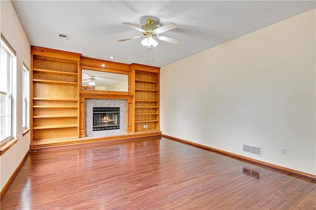 unfurnished living room with ceiling fan, light hardwood / wood-style floors, a textured ceiling, and built in features