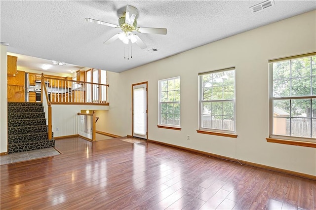 unfurnished living room with ceiling fan, a wealth of natural light, wood-type flooring, and a textured ceiling