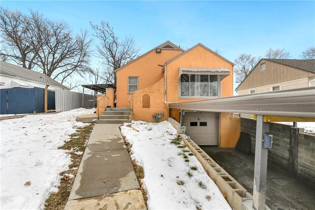 snow covered rear of property with a garage and a carport