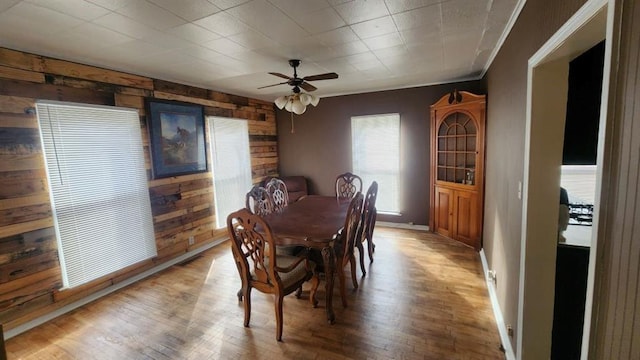 dining space with hardwood / wood-style flooring, ceiling fan, and wood walls