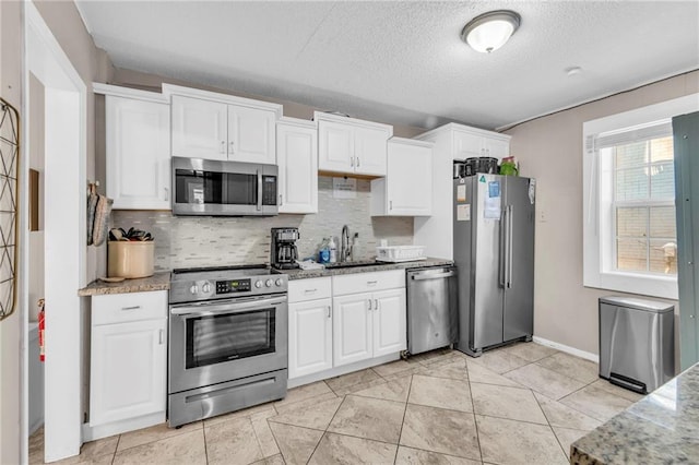 kitchen with sink, white cabinets, light stone counters, stainless steel appliances, and a textured ceiling