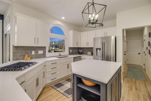 kitchen featuring stainless steel appliances, white cabinetry, sink, and decorative light fixtures