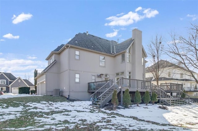 snow covered rear of property with a garage, central AC, and a deck