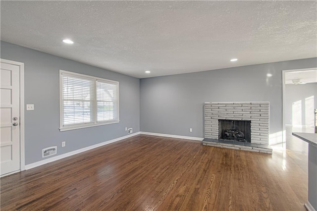 unfurnished living room featuring dark hardwood / wood-style flooring, a brick fireplace, and a textured ceiling