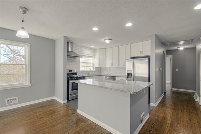 kitchen with a kitchen island, pendant lighting, tasteful backsplash, stainless steel appliances, and wall chimney exhaust hood