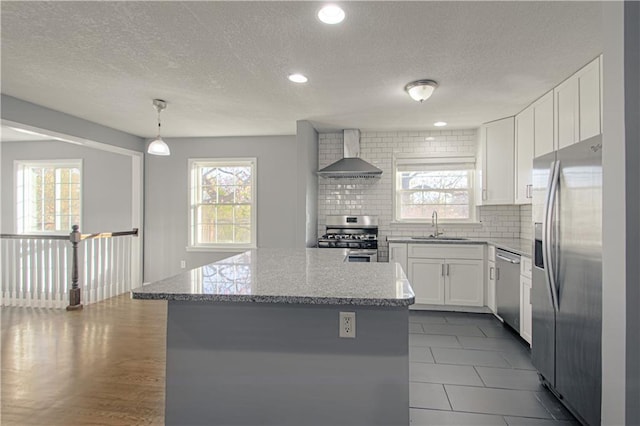 kitchen with wall chimney exhaust hood, stainless steel appliances, a kitchen island, and white cabinets