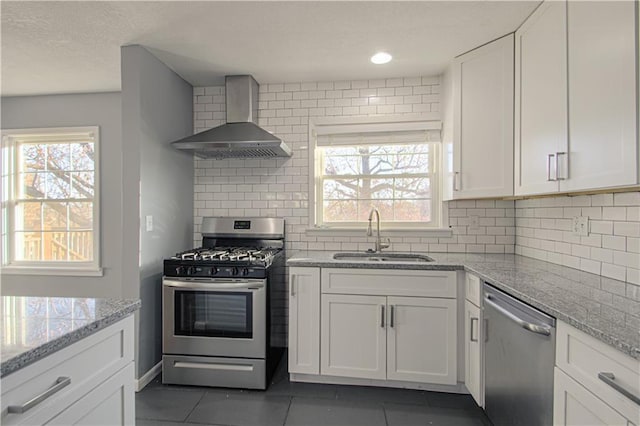 kitchen with wall chimney exhaust hood, sink, white cabinetry, dark tile patterned floors, and stainless steel appliances