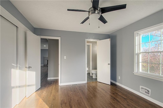 unfurnished bedroom featuring multiple windows, ceiling fan, dark hardwood / wood-style floors, and ensuite bath