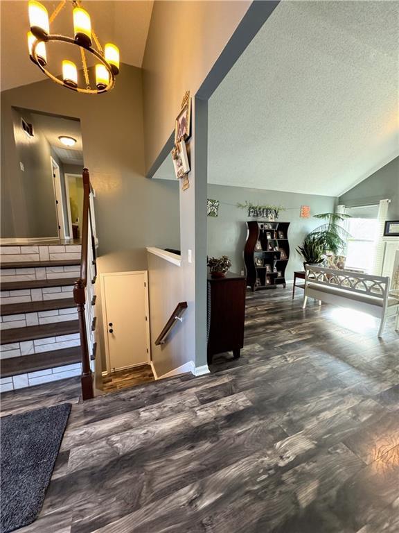 stairway featuring an inviting chandelier, vaulted ceiling, hardwood / wood-style floors, and a textured ceiling