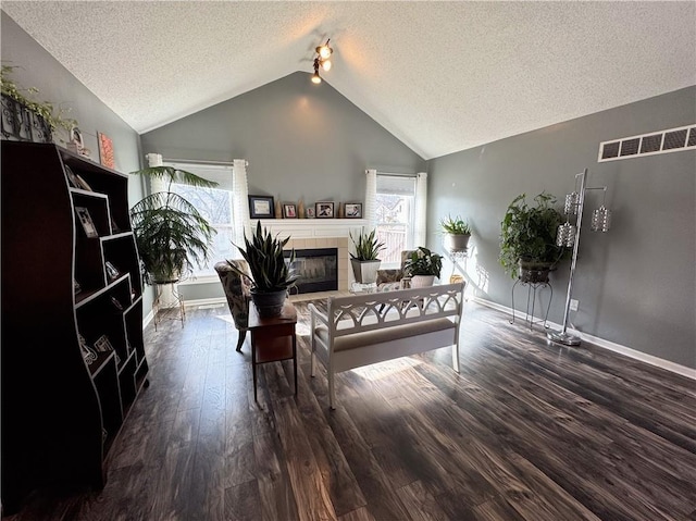 living room with dark hardwood / wood-style flooring, vaulted ceiling, a tile fireplace, and a textured ceiling