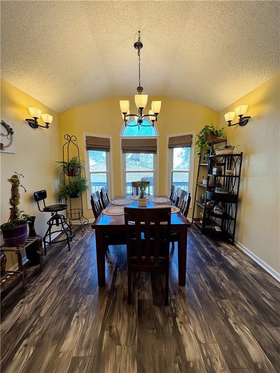 dining space featuring dark hardwood / wood-style flooring, a textured ceiling, vaulted ceiling, and a chandelier