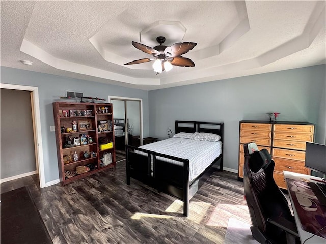 bedroom with ceiling fan, a raised ceiling, dark wood-type flooring, a textured ceiling, and a closet