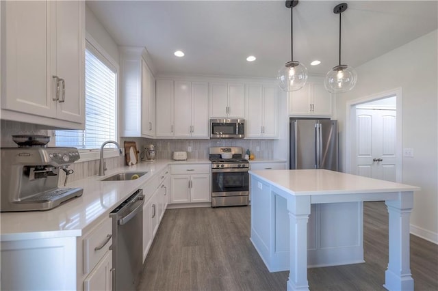kitchen with decorative backsplash, white cabinets, a kitchen island, appliances with stainless steel finishes, and a sink