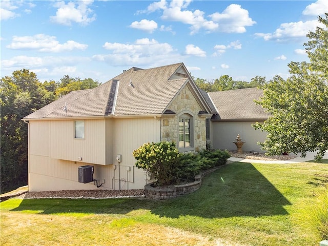 view of side of home with a yard, roof with shingles, stone siding, and central air condition unit