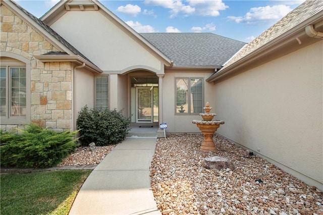 entrance to property featuring stone siding, roof with shingles, and stucco siding