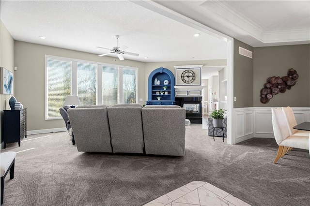 living area featuring a decorative wall, light carpet, a multi sided fireplace, visible vents, and wainscoting