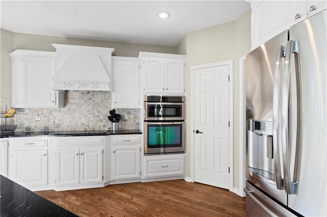 kitchen with custom range hood, appliances with stainless steel finishes, white cabinets, and dark stone counters