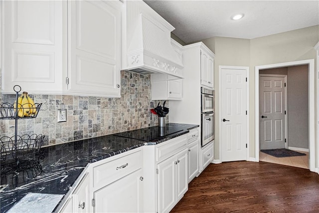 kitchen featuring white cabinets, dark wood finished floors, premium range hood, black electric cooktop, and double oven