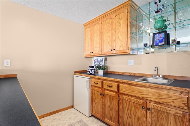 kitchen featuring baseboards, dark countertops, refrigerator, a textured ceiling, and a sink