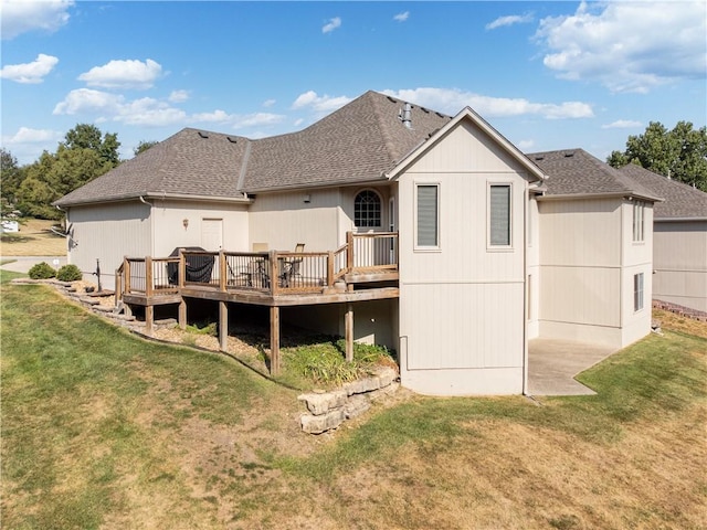 back of house with roof with shingles, a lawn, and a wooden deck