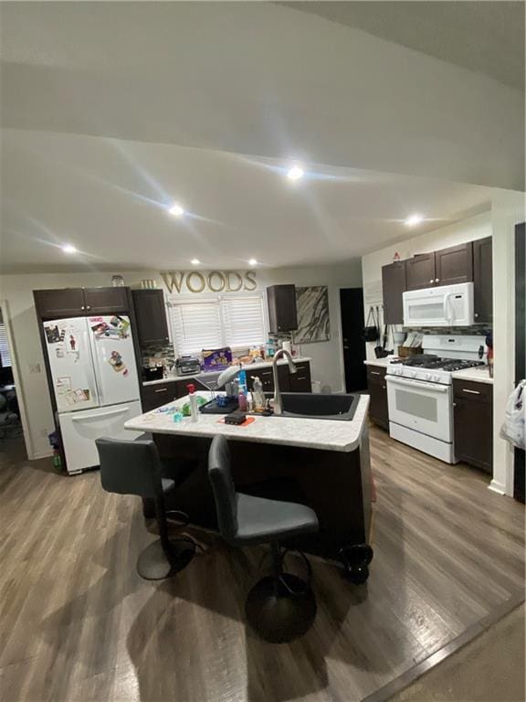 kitchen with sink, white appliances, light hardwood / wood-style flooring, dark brown cabinets, and an island with sink