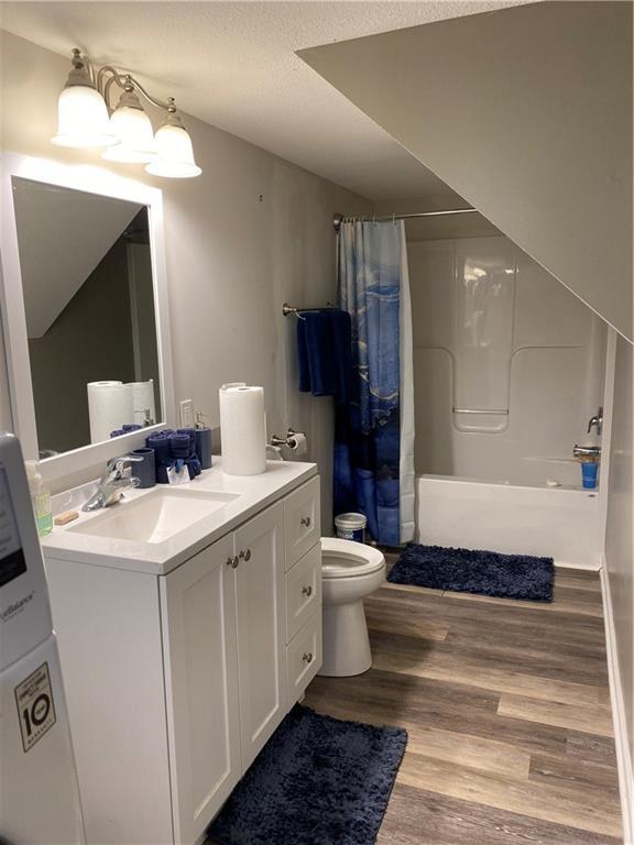 full bathroom featuring hardwood / wood-style flooring, vanity, shower / tub combo with curtain, and toilet