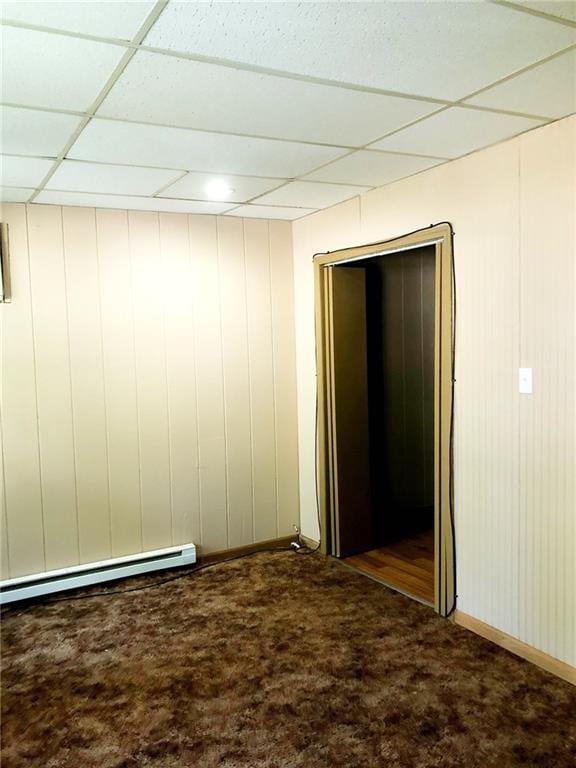 corridor with a baseboard heating unit, a paneled ceiling, and dark colored carpet