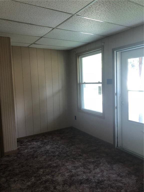 carpeted spare room with wooden walls and a drop ceiling