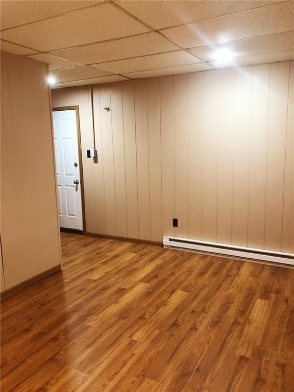 unfurnished room with hardwood / wood-style floors, a paneled ceiling, wooden walls, and baseboard heating