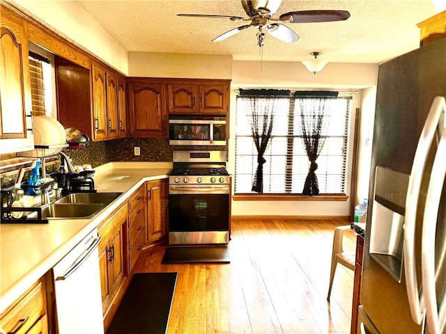 kitchen featuring sink, light wood-type flooring, decorative backsplash, stainless steel appliances, and a textured ceiling