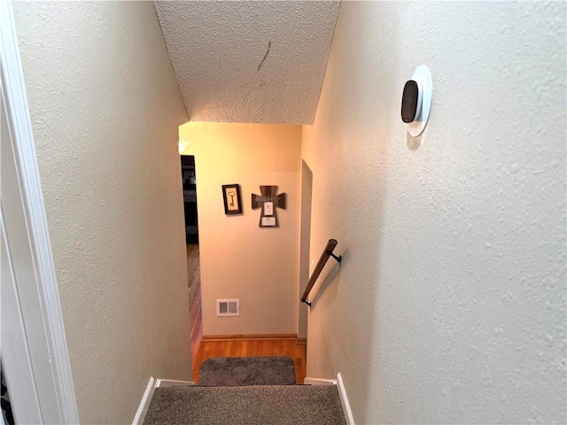 stairs featuring a textured ceiling and carpet flooring