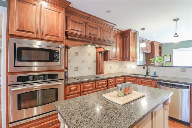 kitchen with light stone counters, stainless steel appliances, sink, and hanging light fixtures