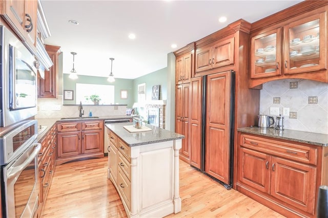 kitchen with sink, built in appliances, decorative light fixtures, dark stone countertops, and a kitchen island