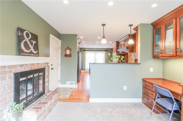 kitchen with decorative light fixtures, light carpet, a brick fireplace, stainless steel fridge, and kitchen peninsula