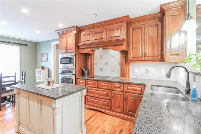 kitchen featuring sink, appliances with stainless steel finishes, a kitchen island, light stone countertops, and light hardwood / wood-style floors