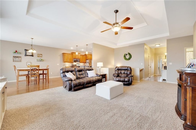 living room with light carpet, ceiling fan, and a raised ceiling