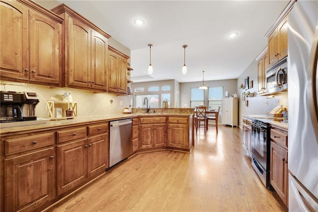 kitchen with appliances with stainless steel finishes, sink, decorative light fixtures, light hardwood / wood-style floors, and decorative backsplash